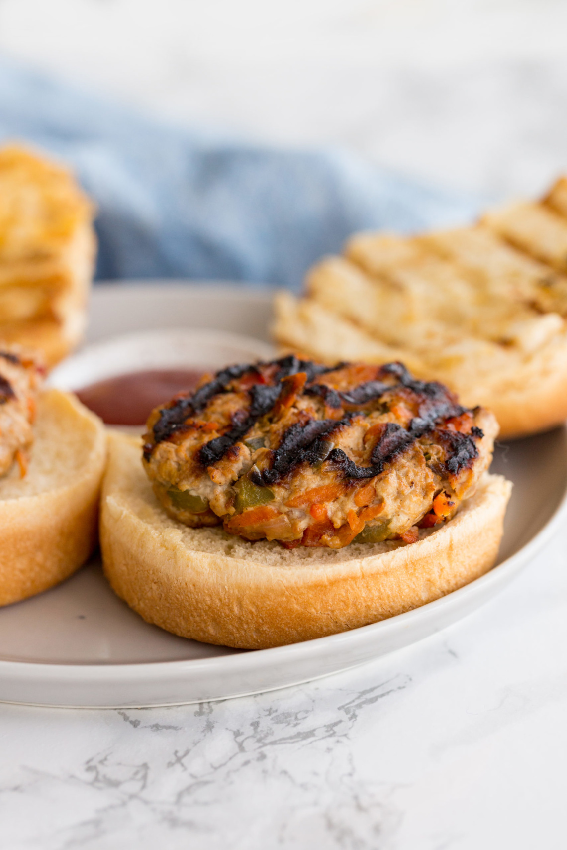Stacked grilled turkey burgers on whole grain buns showing visible char marks, melted Swiss cheese, fresh lettuce, sliced tomato, and red onion, with the burger's hidden grated zucchini and carrots invisible in the patty, set on a wooden cutting board.